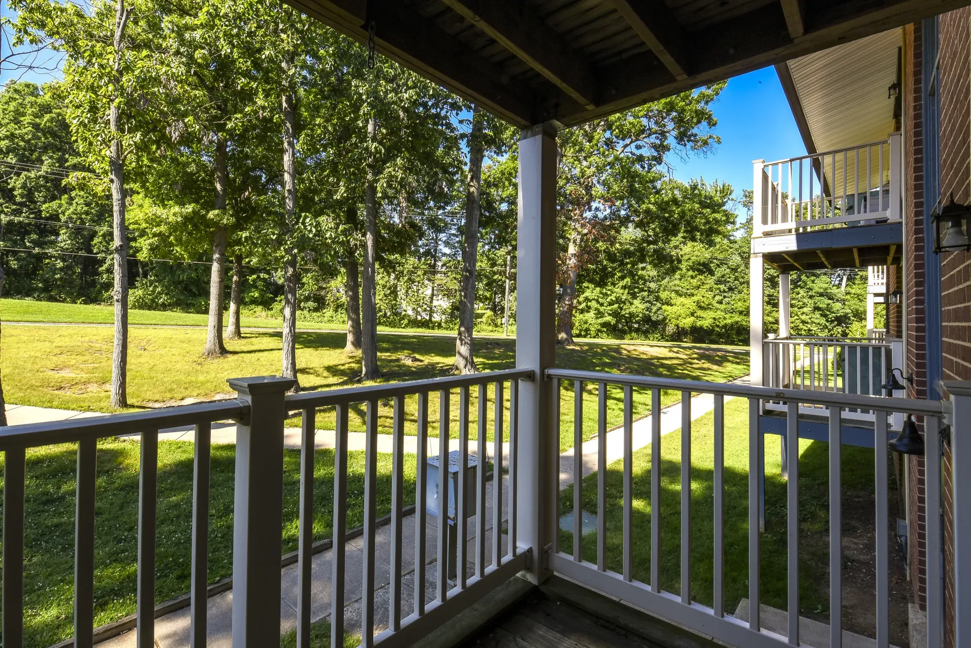 View from a second-story balcony of a courtyard with grass, trees, and neighboring balconies.