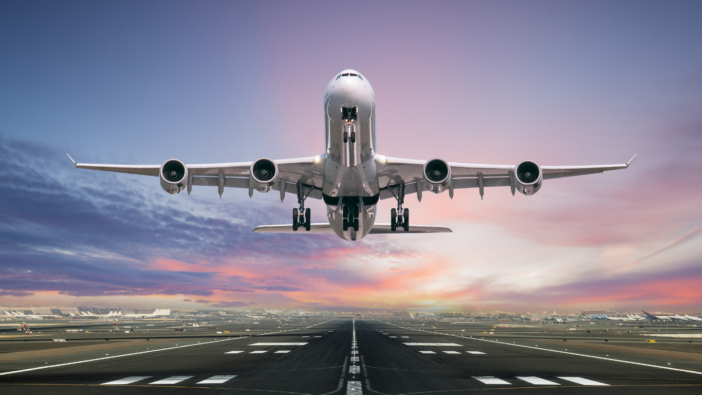 A large passenger jet is taking off from an airport runway at sunset.