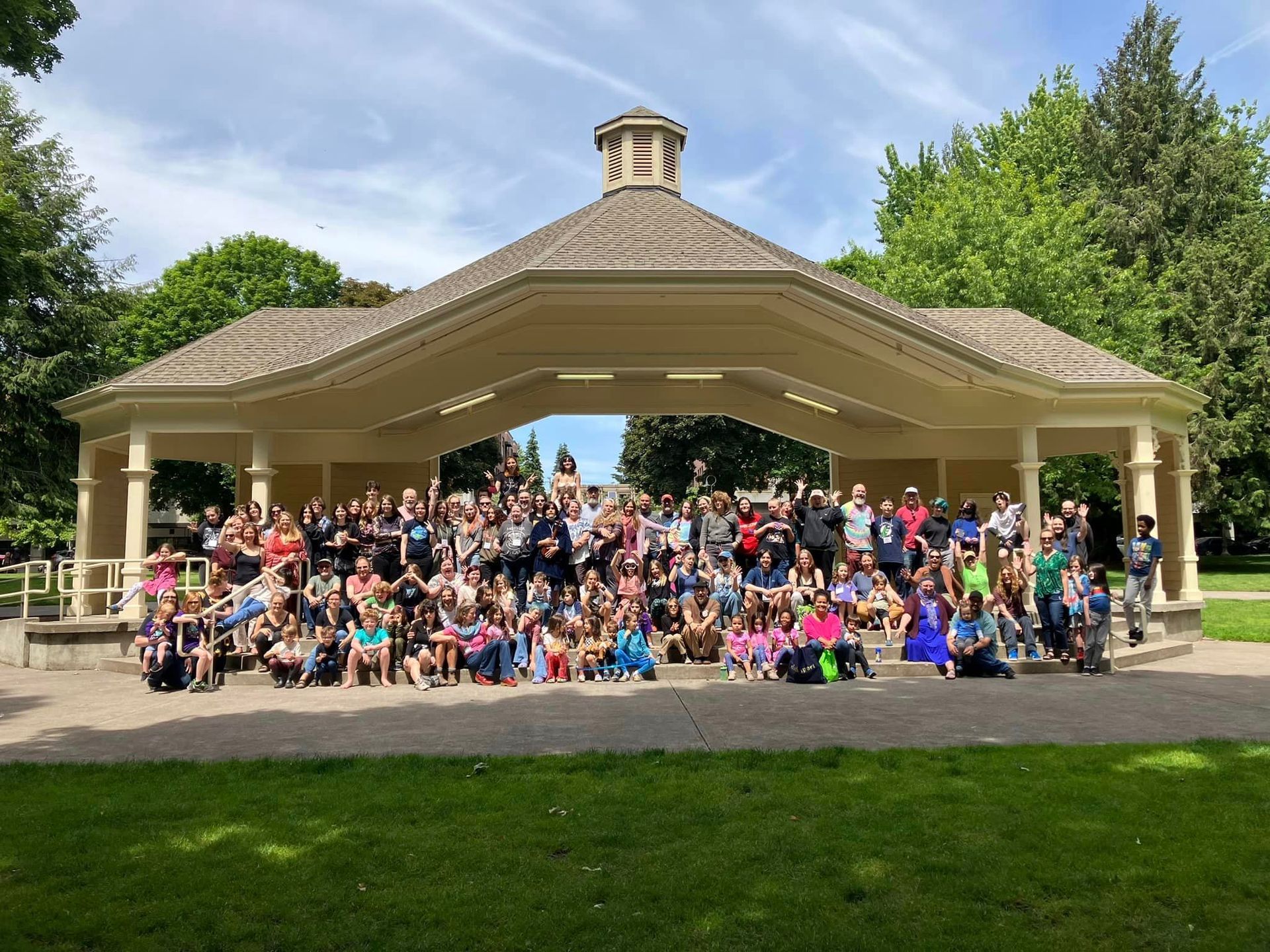 A large group of people are posing for a picture in front of a gazebo in a park.