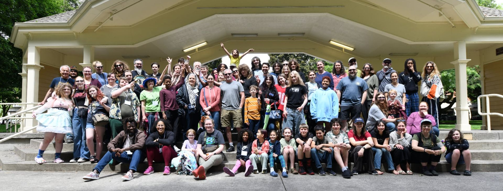 Group of people posing for a photo on steps in front of a beige pavilion with trees in the background.