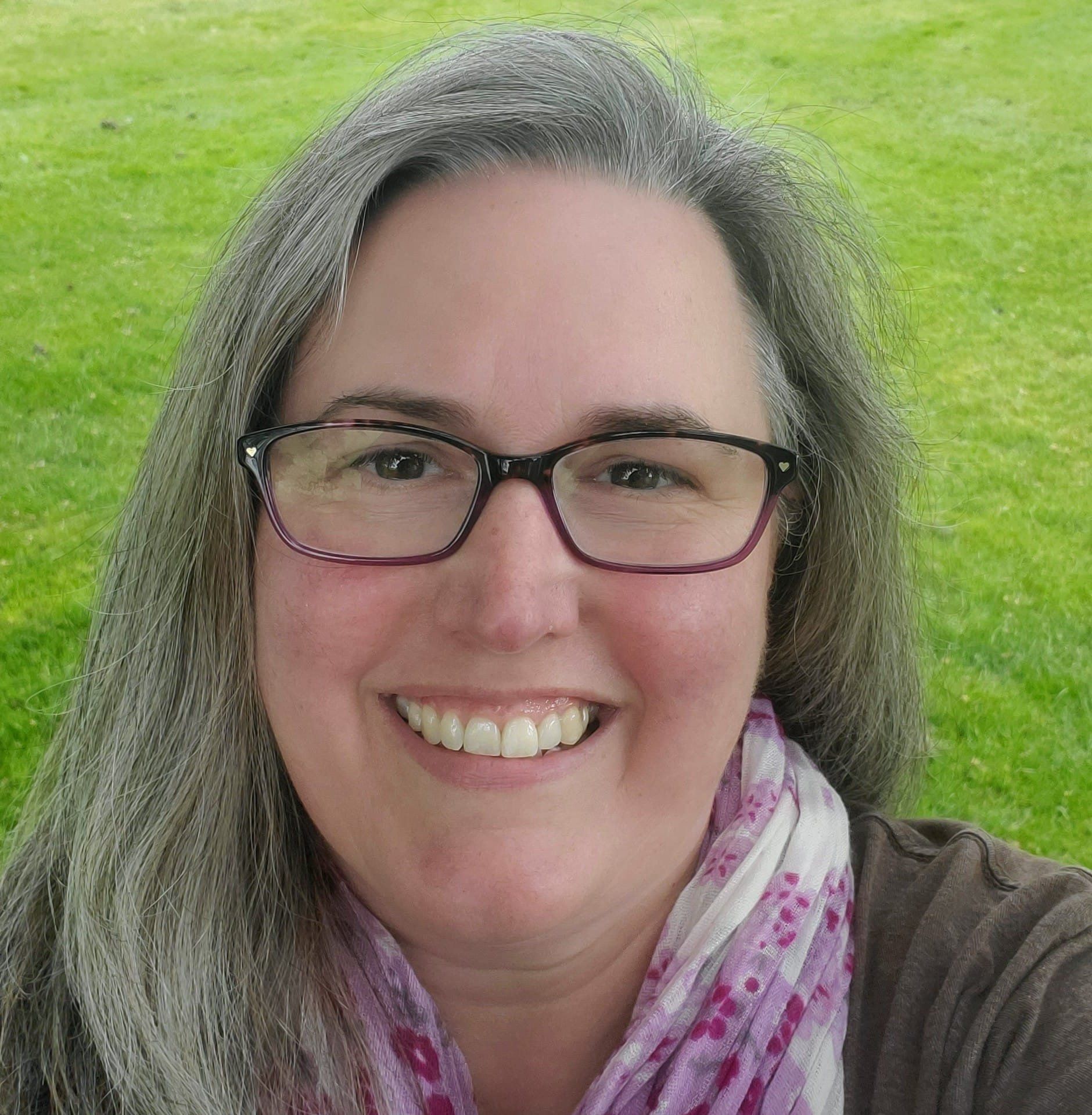 Chrissie Korolsky, a woman wearing glasses and a scarf is smiling for the camera. 