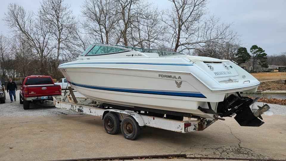 A red truck is towing a white boat on a trailer.