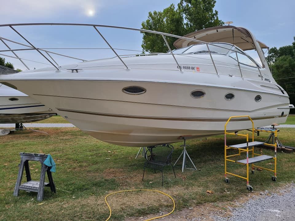 A white boat is parked in the grass next to a yellow ladder.