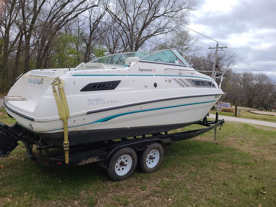 A white boat is parked on a trailer in a grassy field.