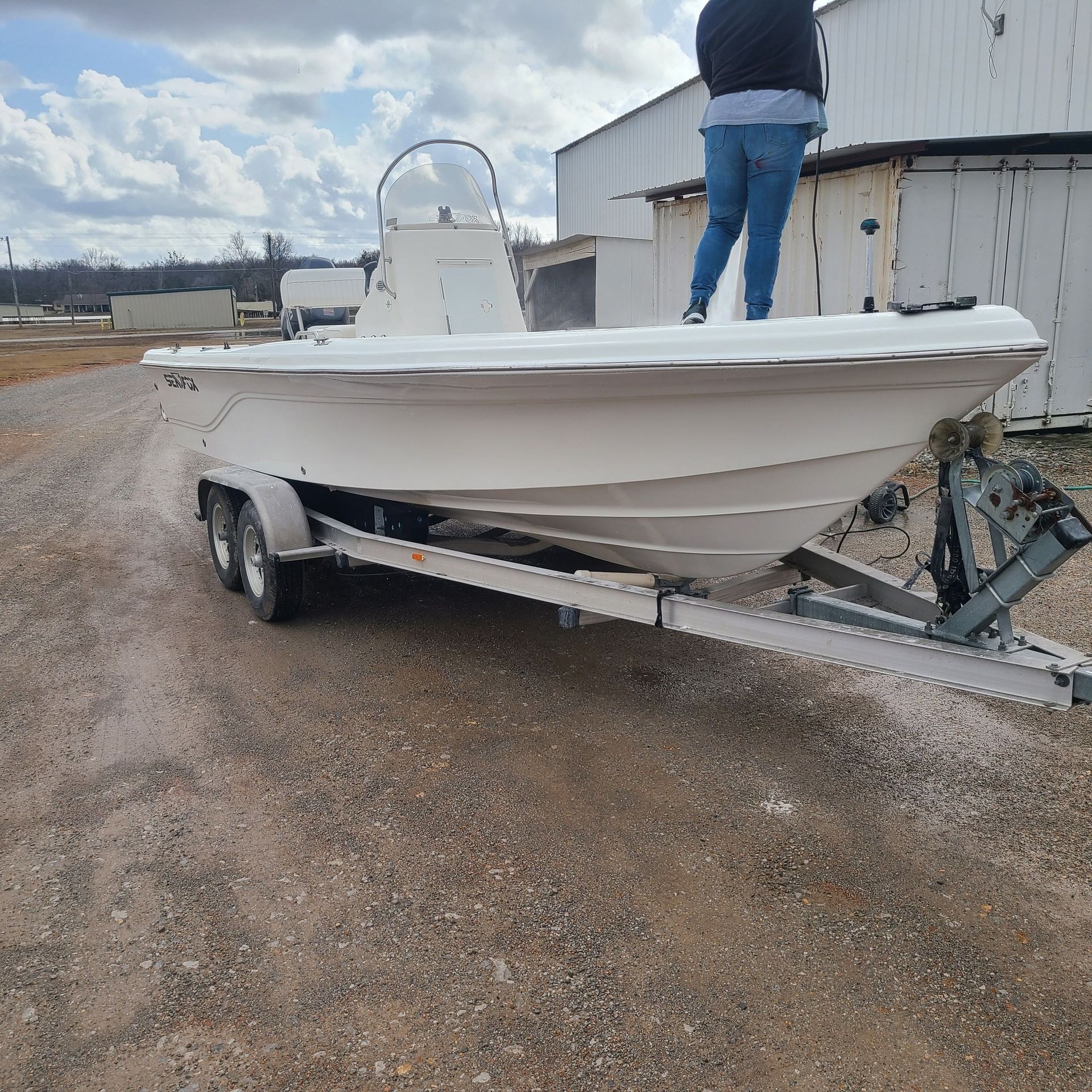 A man is standing on top of a white boat on a trailer.