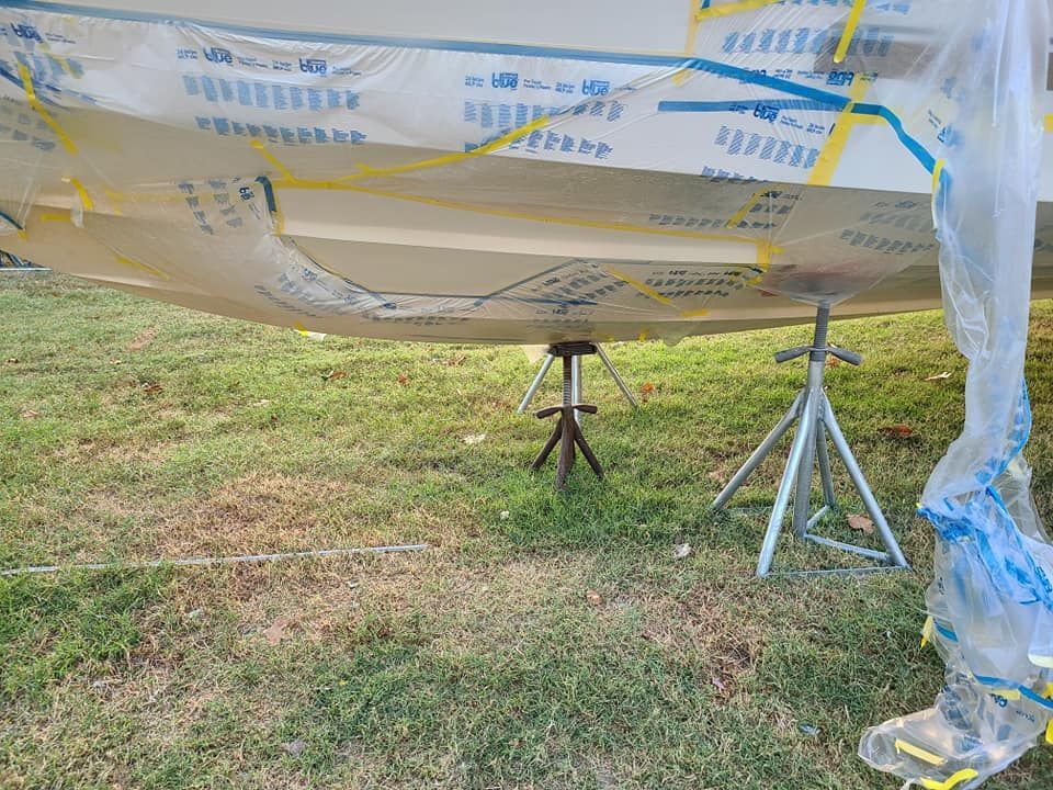 A boat is wrapped in plastic and sitting on a stand in the grass.