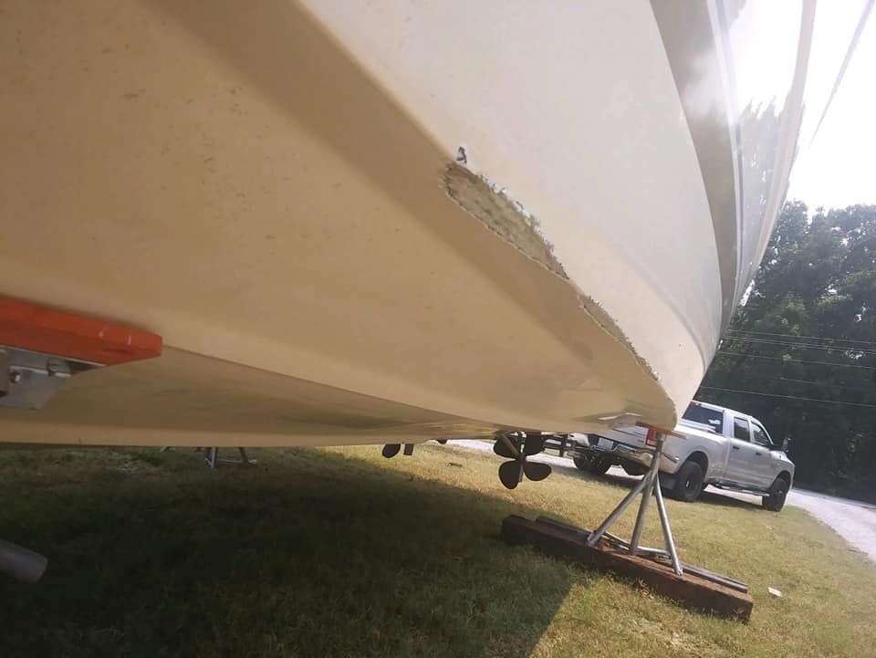 The bottom of a boat is sitting on a wooden stand in the grass.