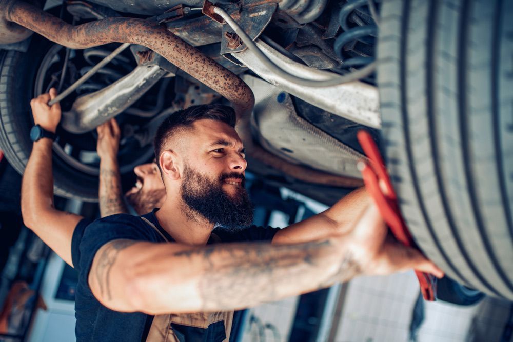 A Man Is Working Under A Car In A Garage — CAL AUTO Mobile Roadworthys in Childers, QLD