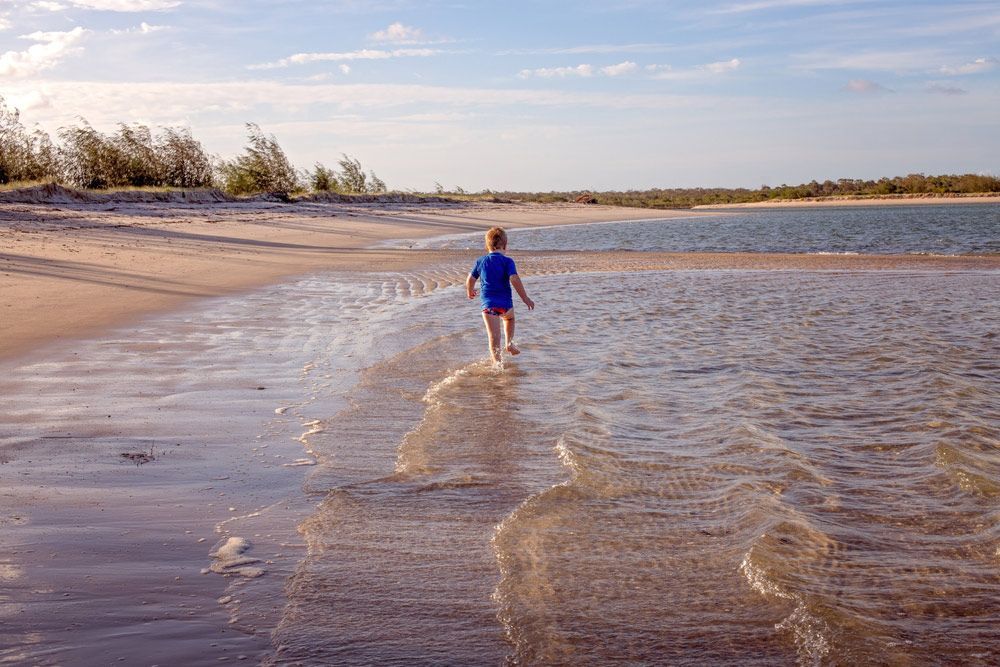 A Young Boy Is Walking On The Beach Near The Water — CAL AUTO Mobile Roadworthys in Woodgate, QLD