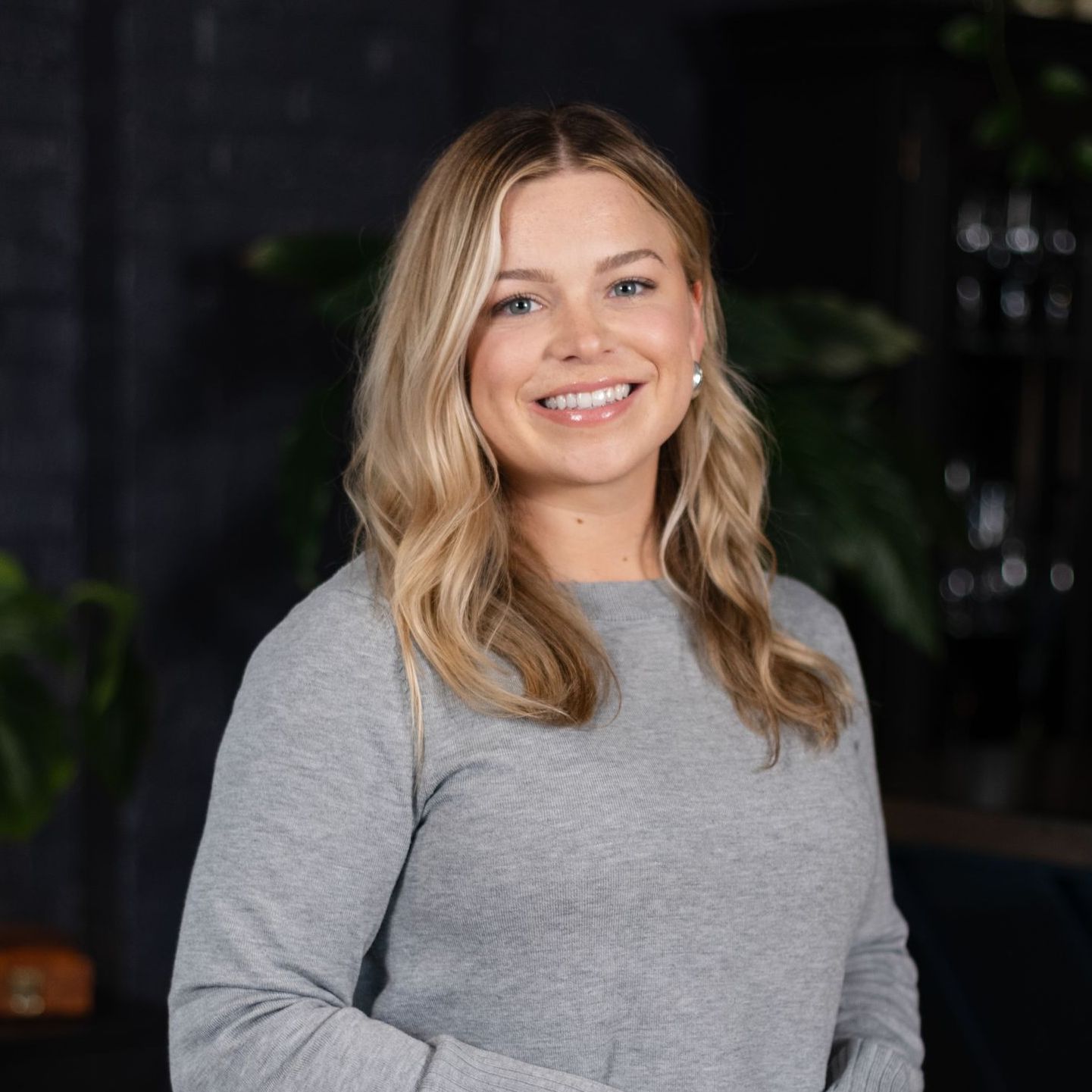 A woman in a grey sweater is smiling for the camera.