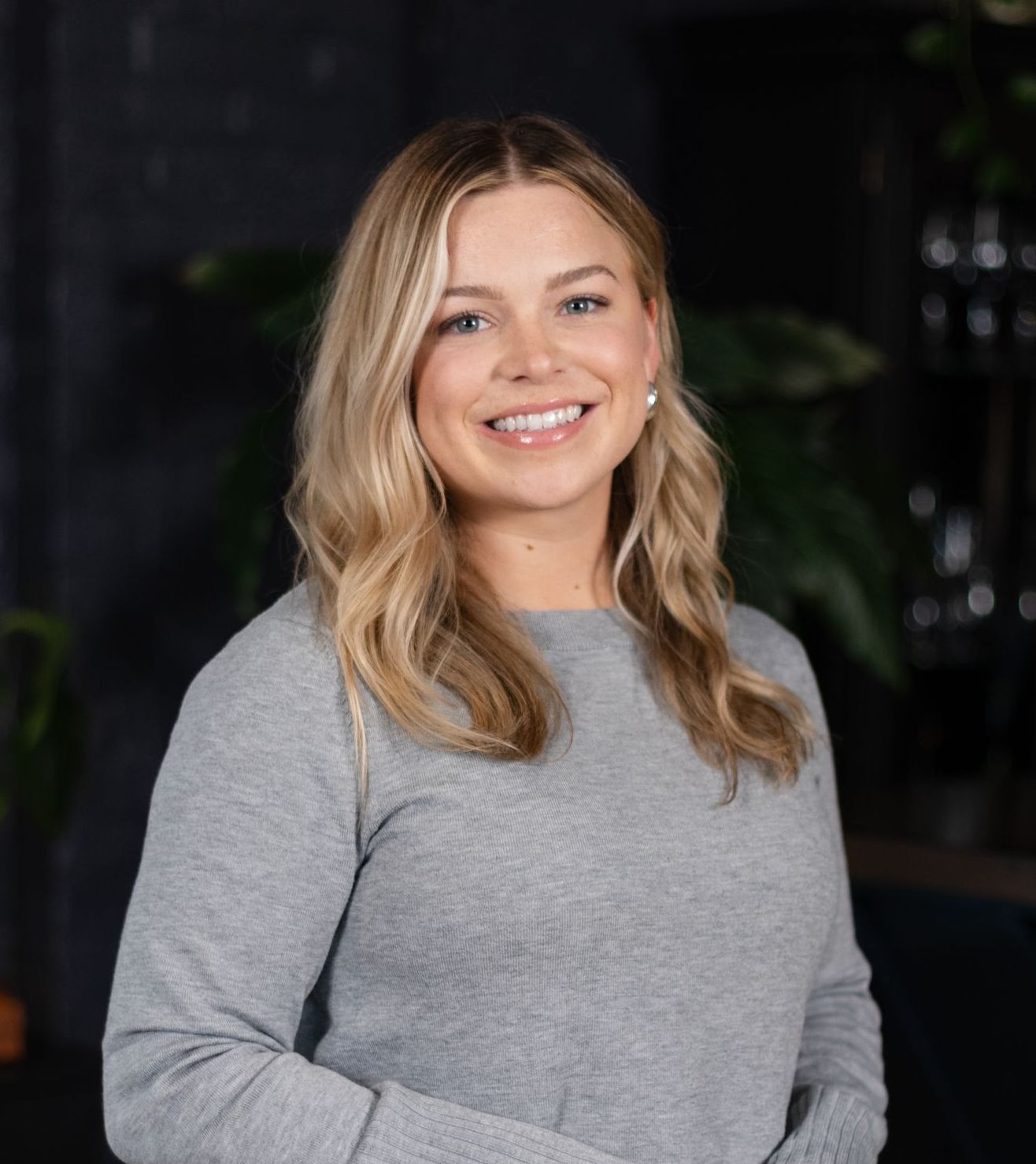 A woman is sitting on a stool with her legs crossed and smiling.