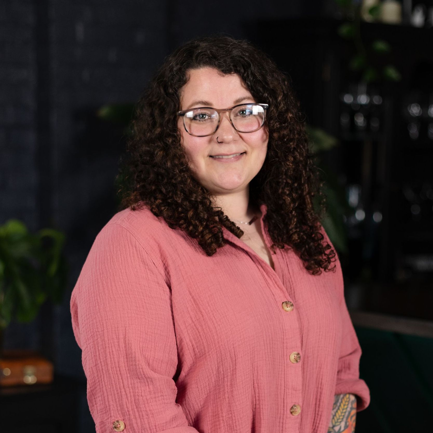 A woman wearing glasses and a blue and white dress is standing with her hands in her pockets.