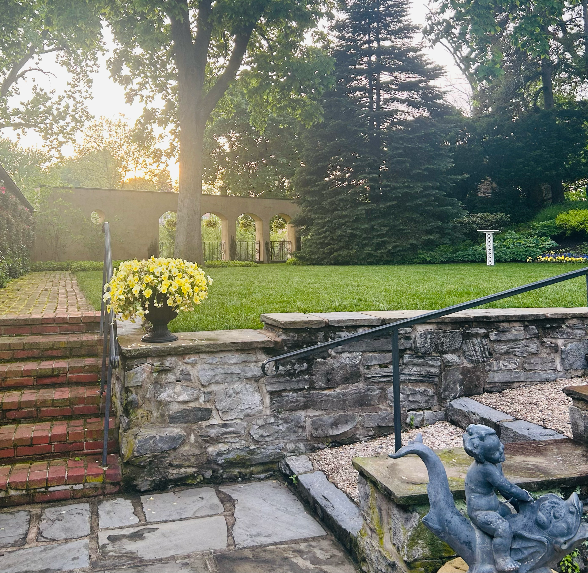 A stone wall with stairs leading up to a lush green field in Conestoga Garden in Lancaster