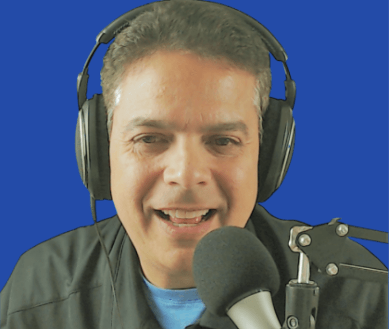 A man wearing headphones is smiling in front of a microphone