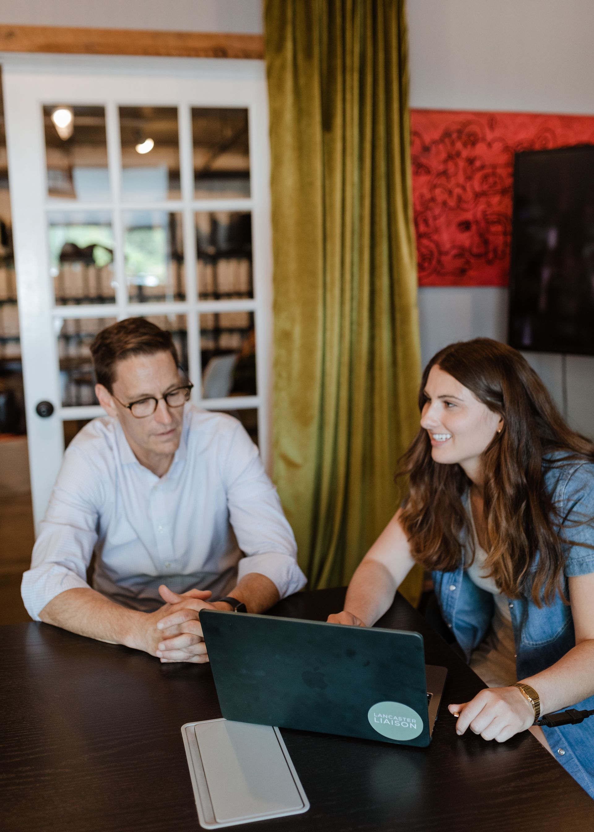 A man and a woman are sitting at a table looking at a laptop.