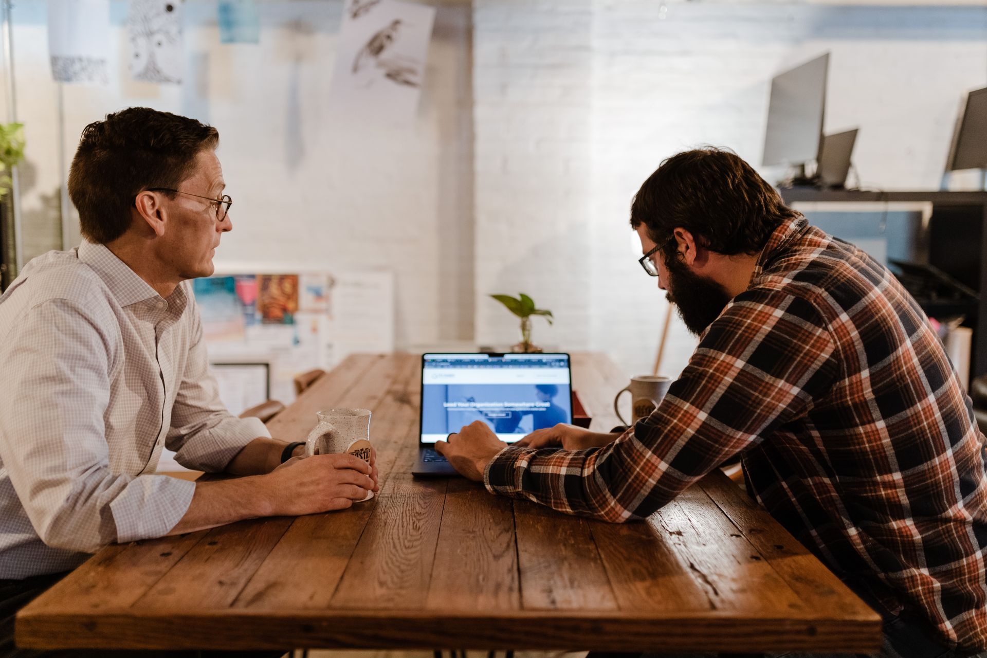 Two men are sitting at a table looking at a laptop.