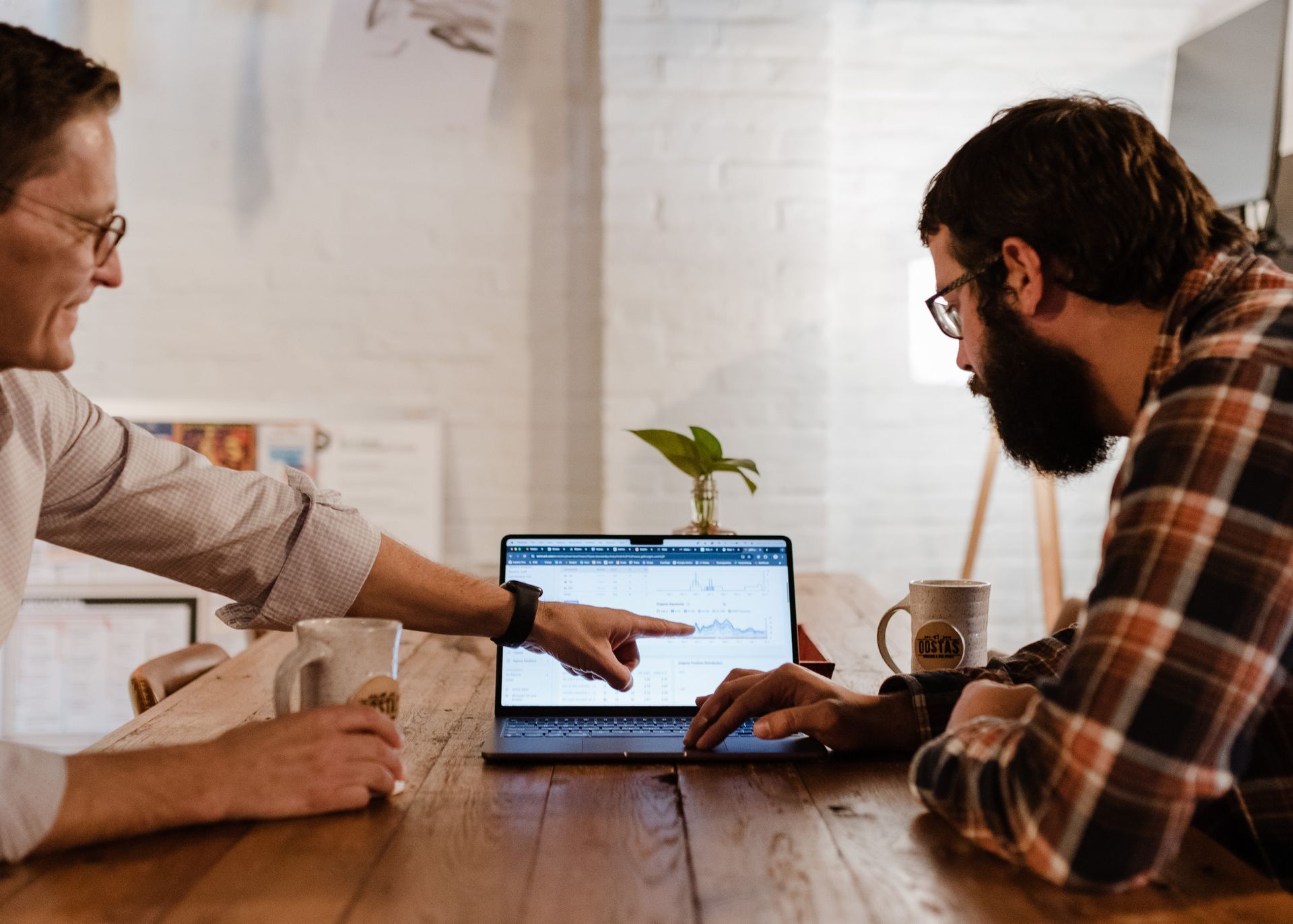 Two men are sitting at a table looking at a laptop computer.