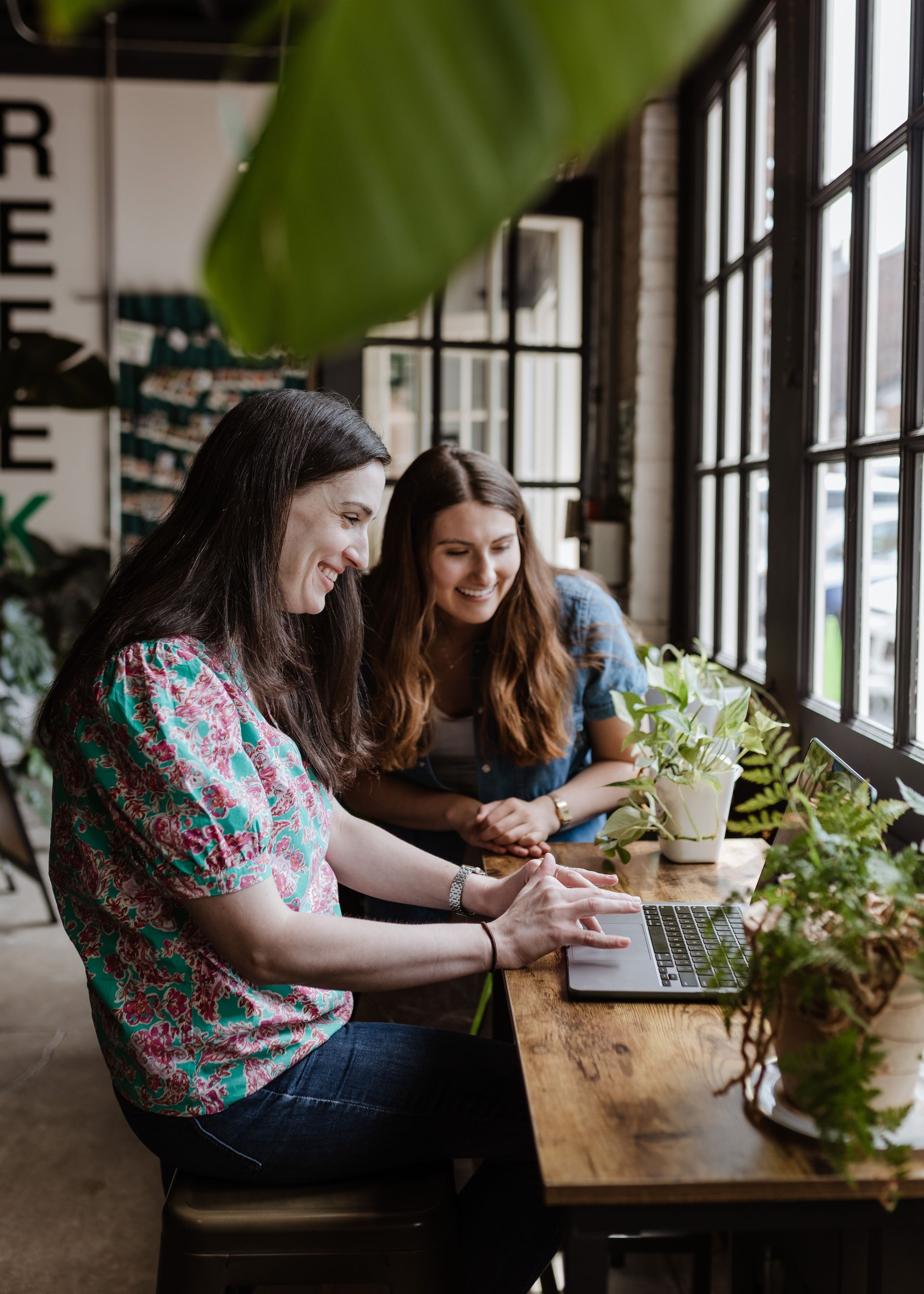 Two women are sitting at a table looking at a laptop.