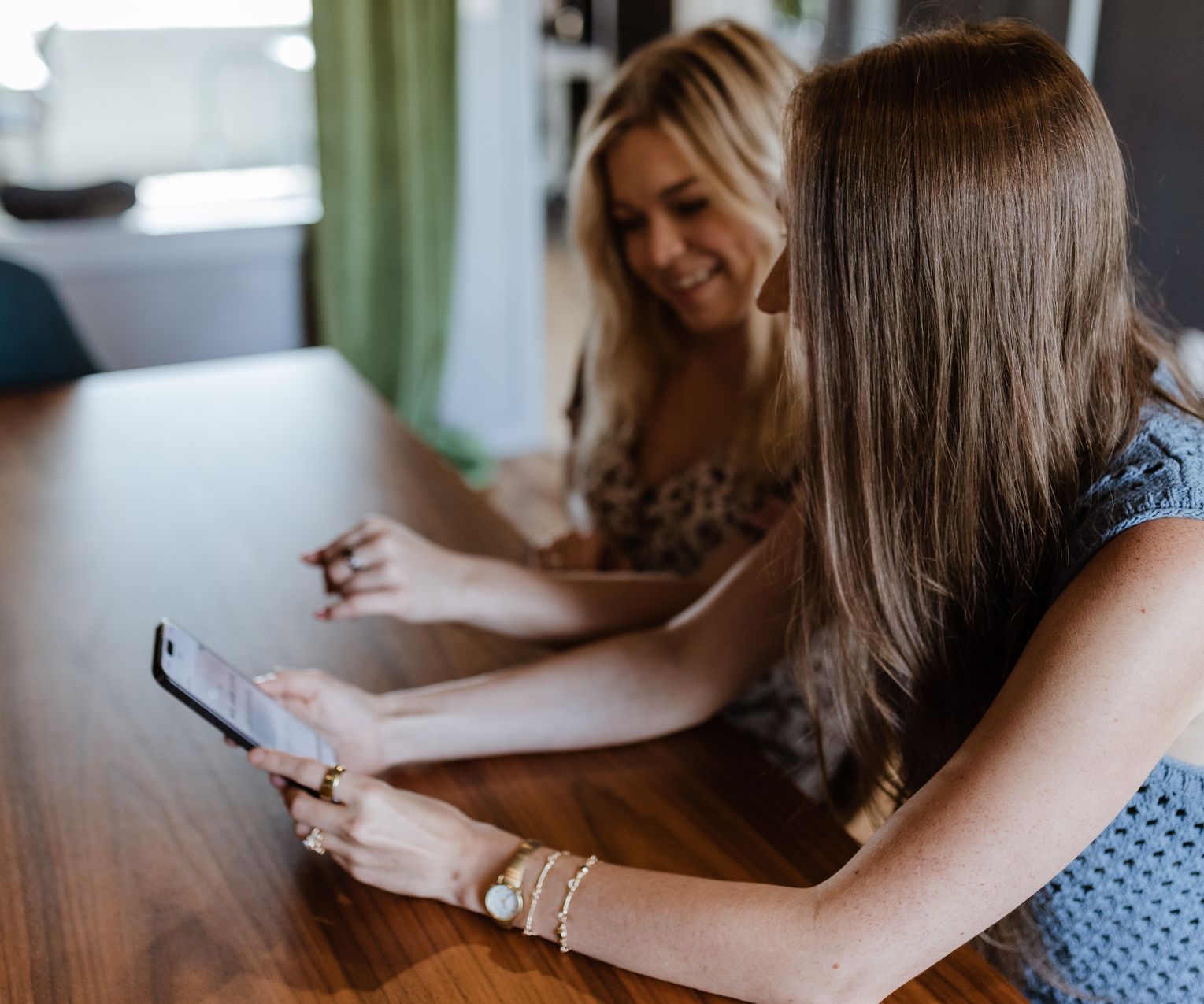 Two women are sitting at a table looking at a tablet.