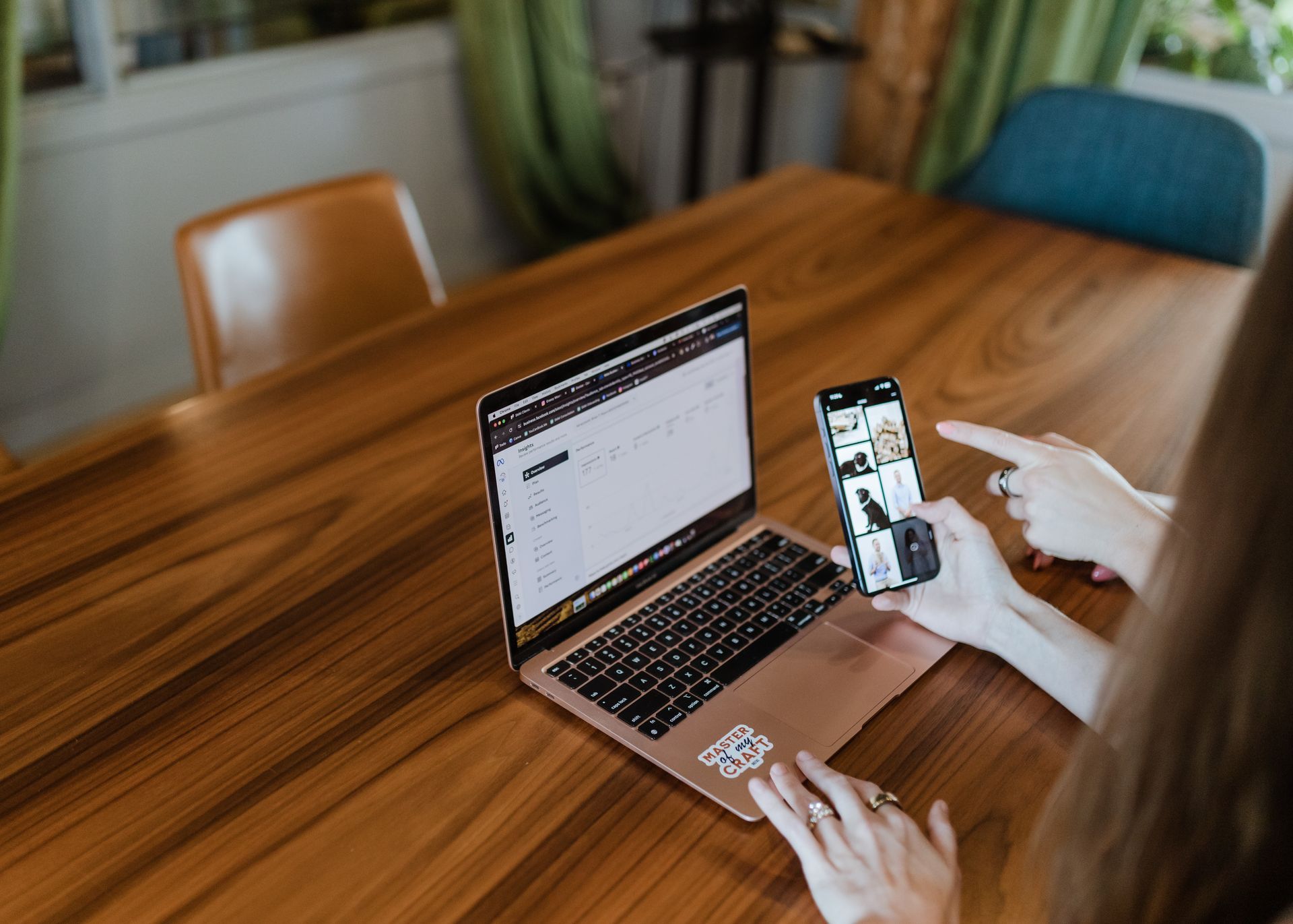 A woman is sitting at a table using a laptop and a cell phone.