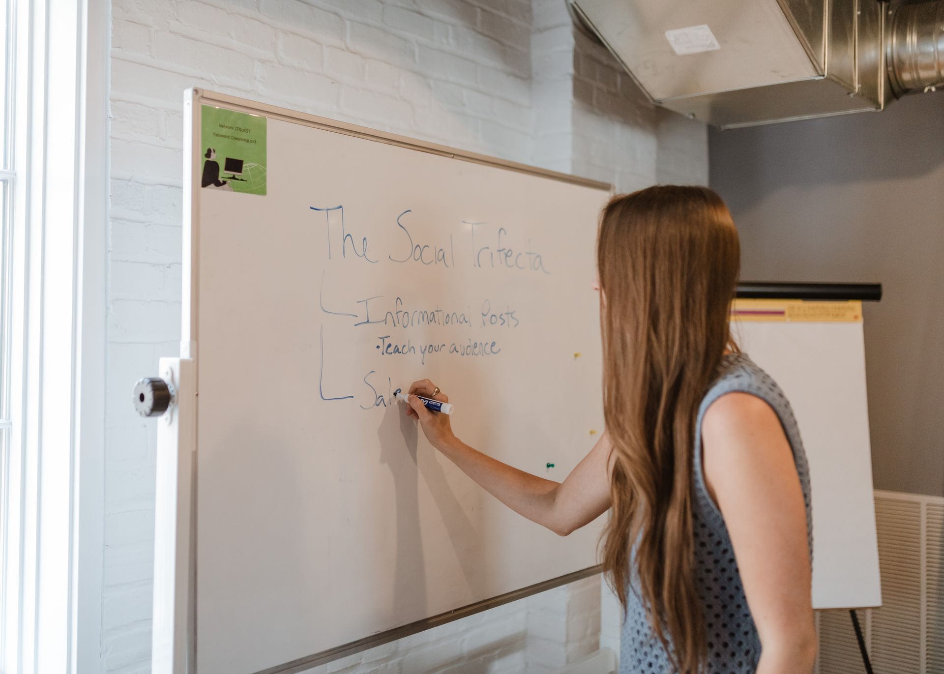 A woman is writing on a whiteboard in a room.