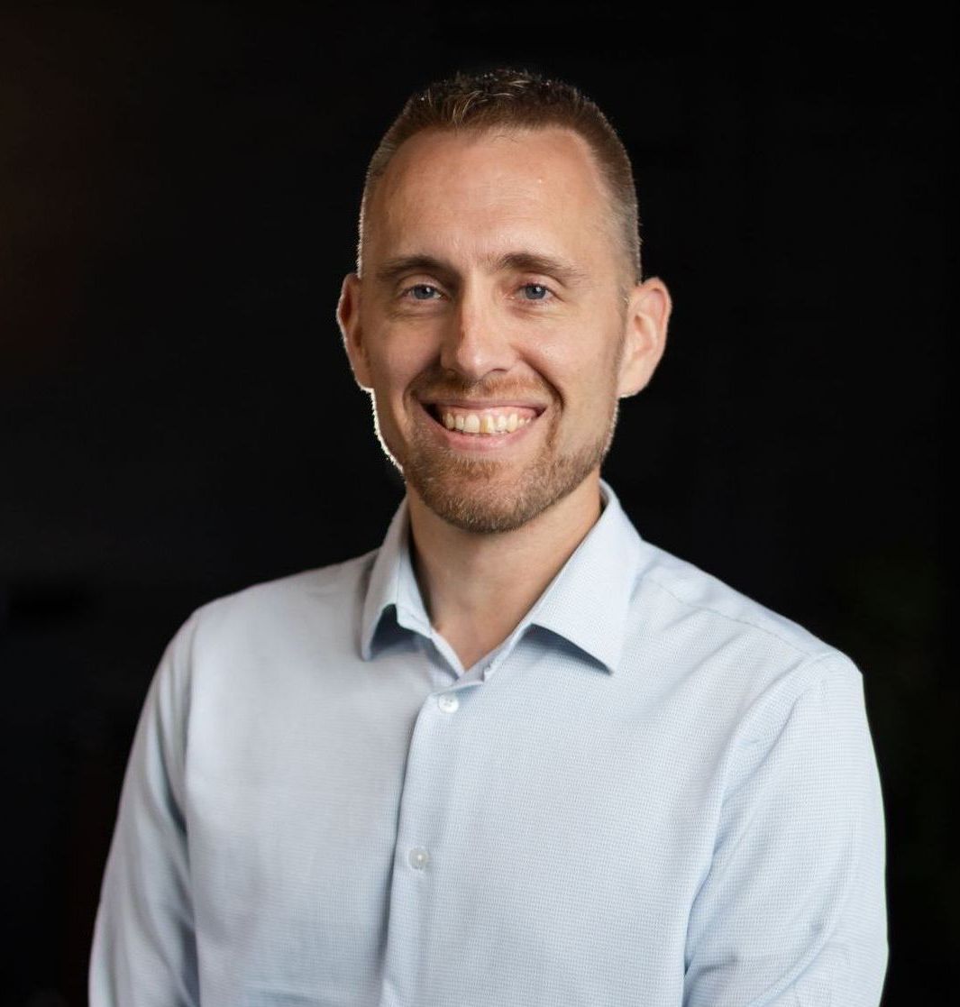 A man in a light blue shirt is smiling for the camera.