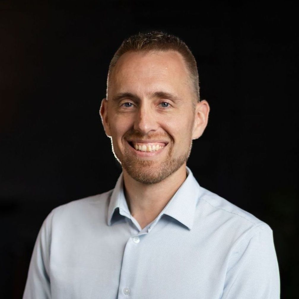 A man with a beard is smiling for the camera while wearing a light blue shirt.