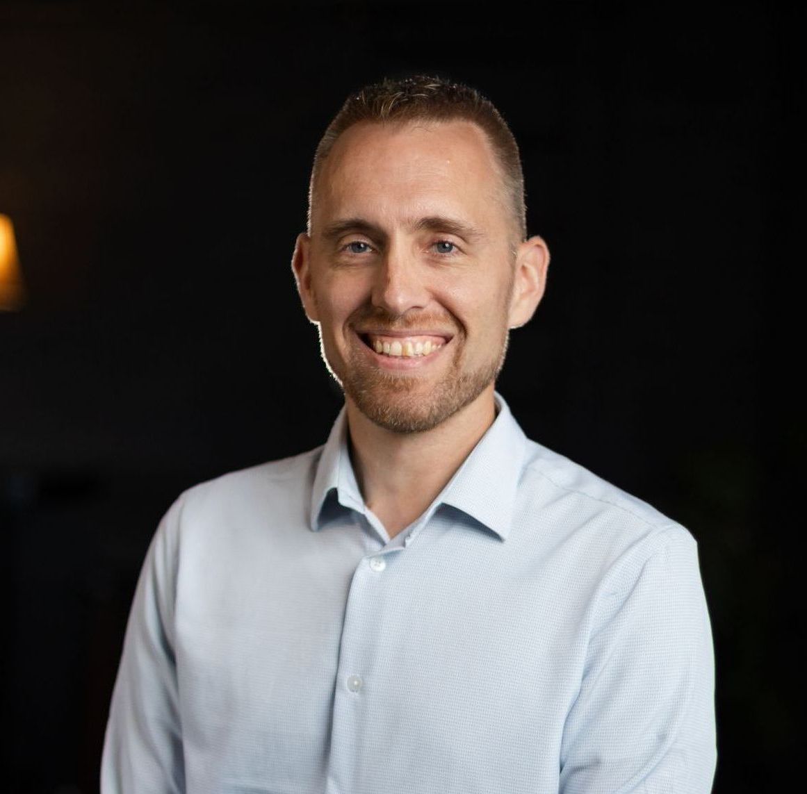 A man in a light blue shirt is smiling for the camera.