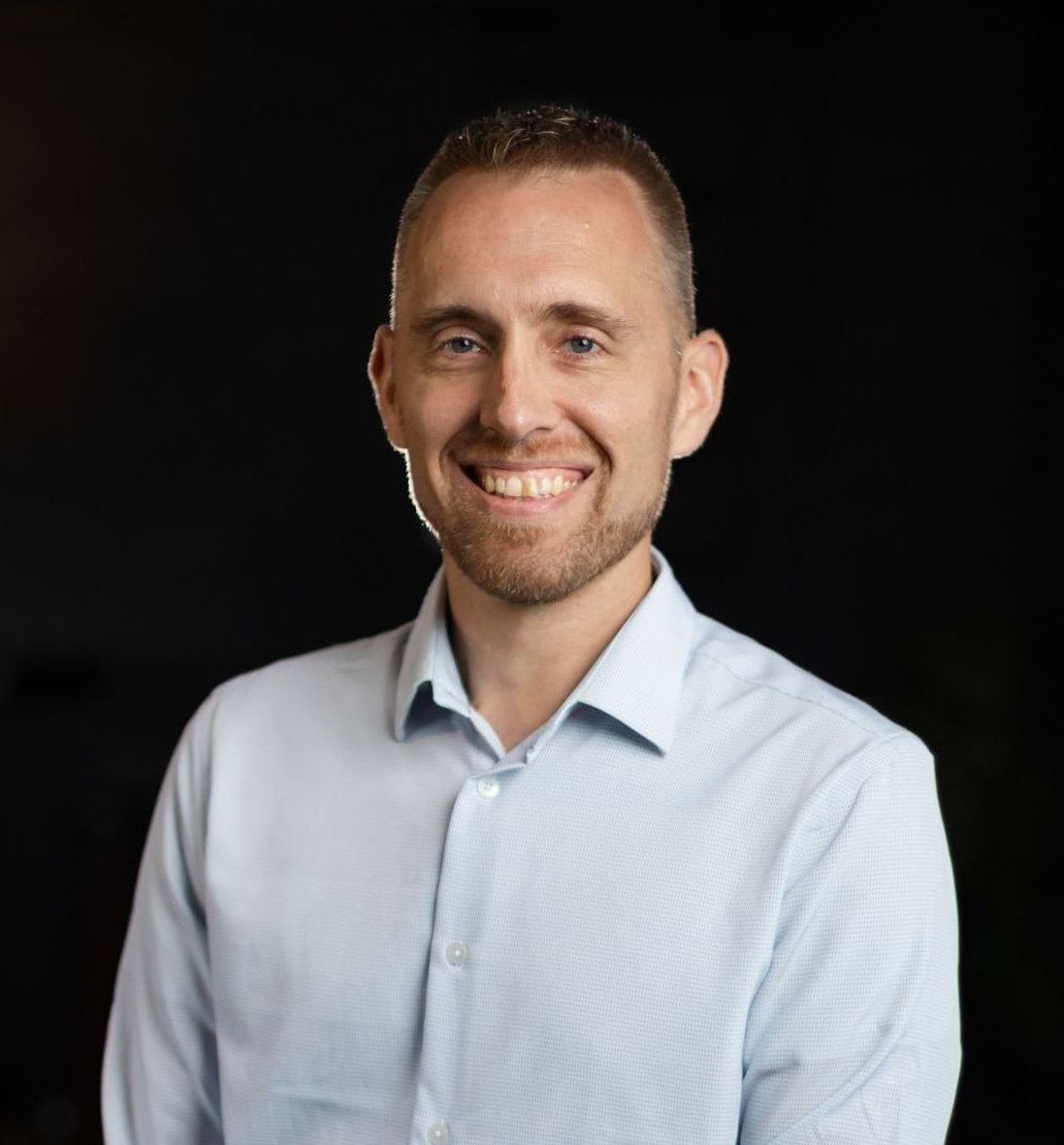 A man in a light blue shirt is smiling for the camera.