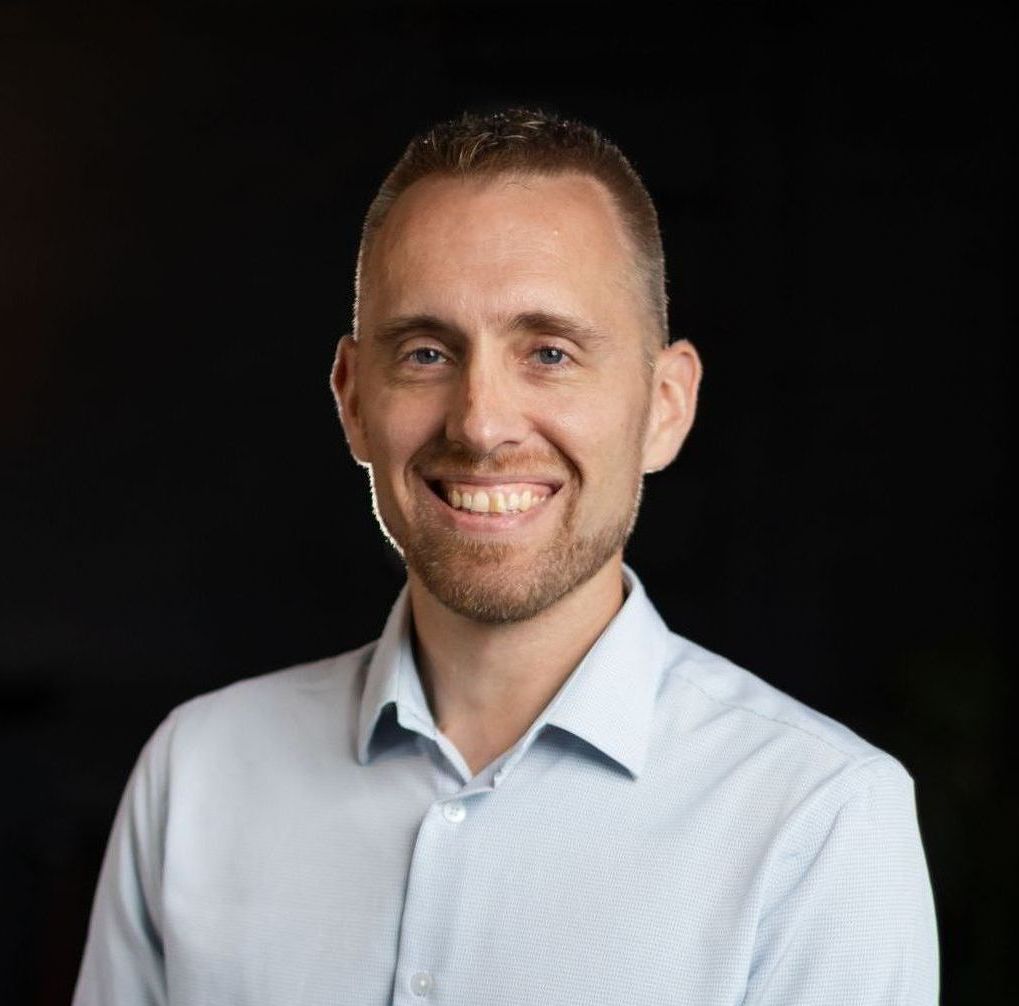 A man with a beard is smiling for the camera while wearing a blue shirt.