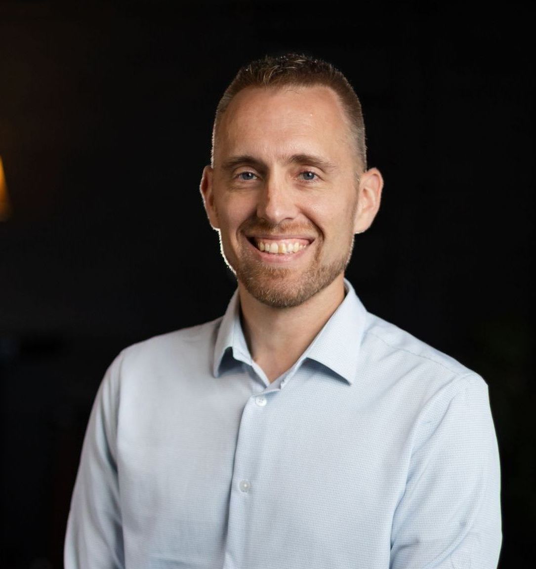 A man in a light blue shirt is smiling for the camera.