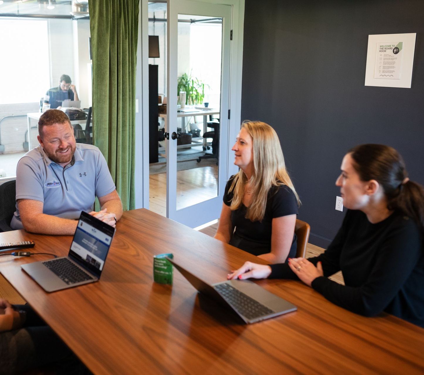 A group of people are sitting around a table with laptops.