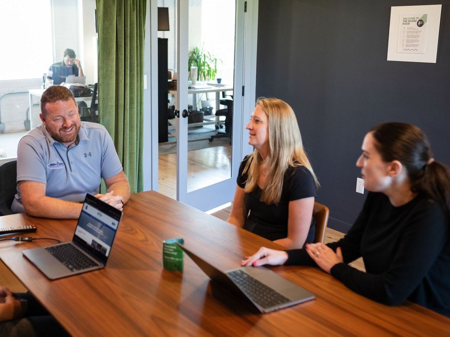 A group of people are sitting around a table with laptops.