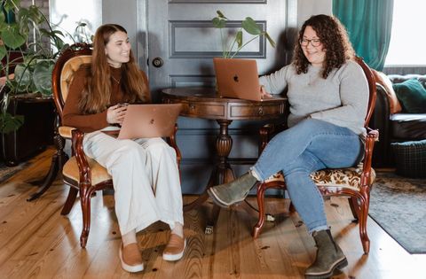 Two women are sitting in chairs looking at laptops.