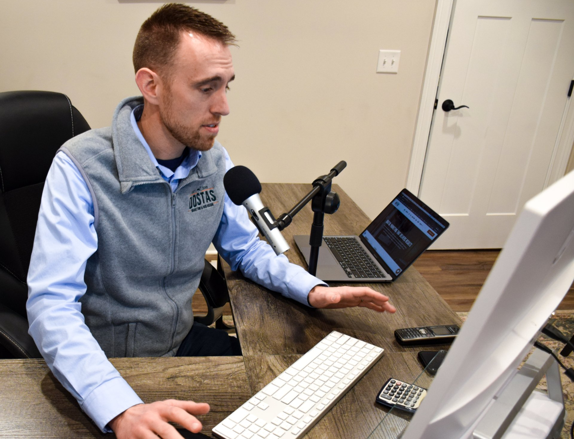 A man is sitting at a desk with a laptop and a microphone.