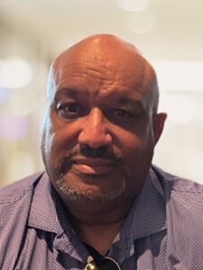 A bald man with a beard is wearing a purple shirt and sunglasses.