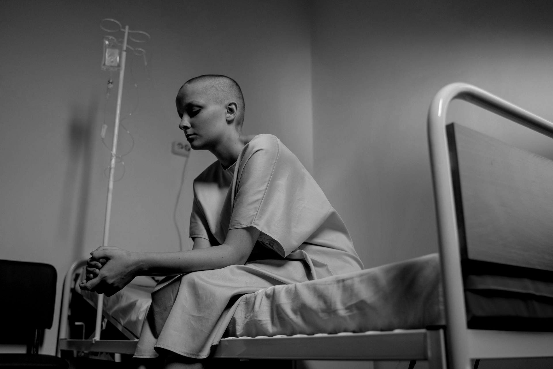 A woman with cancer is sitting on a hospital bed.