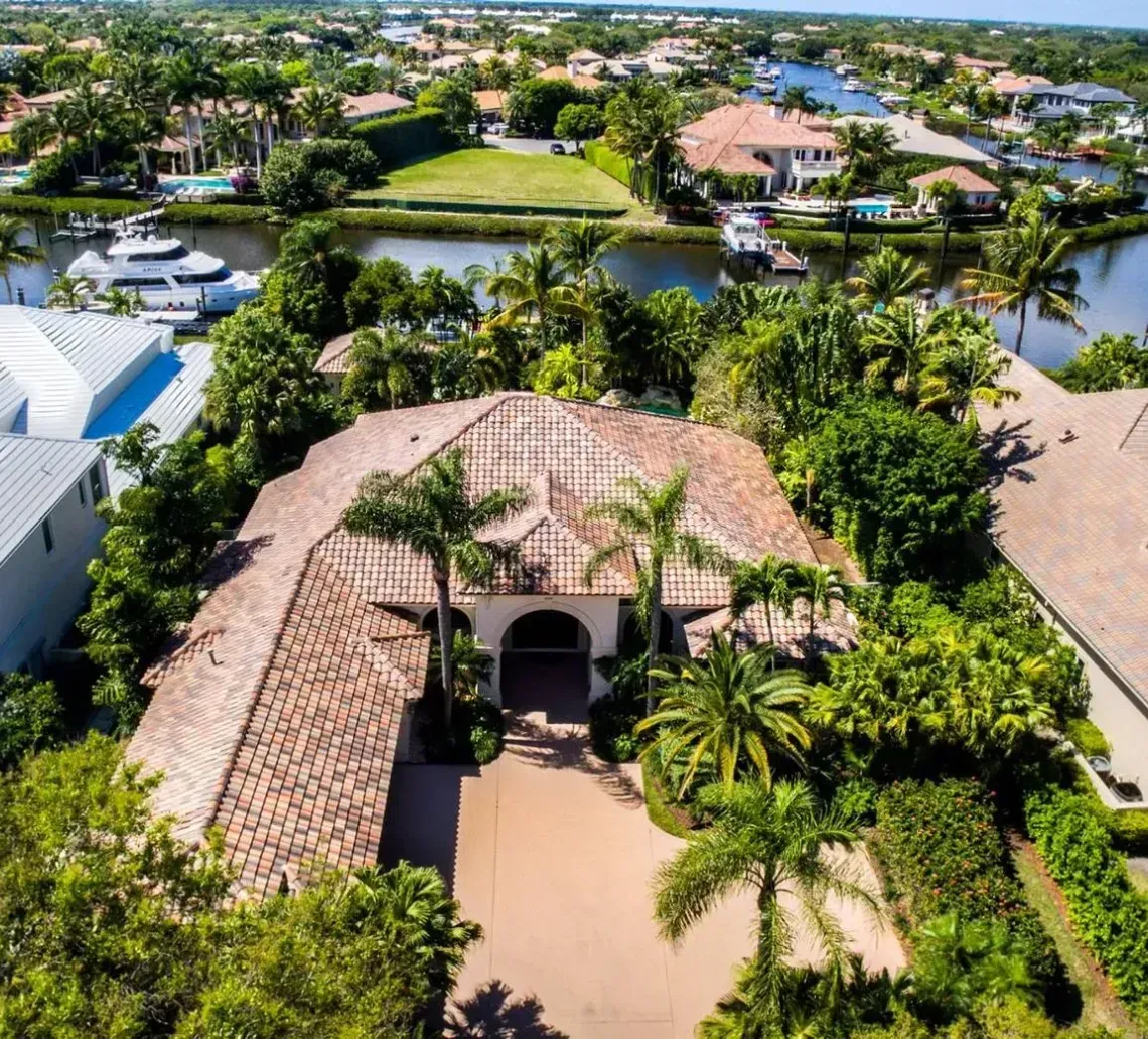Aerial view of a coastal neighborhood with large houses, palm trees, and a canal with a moored boat.