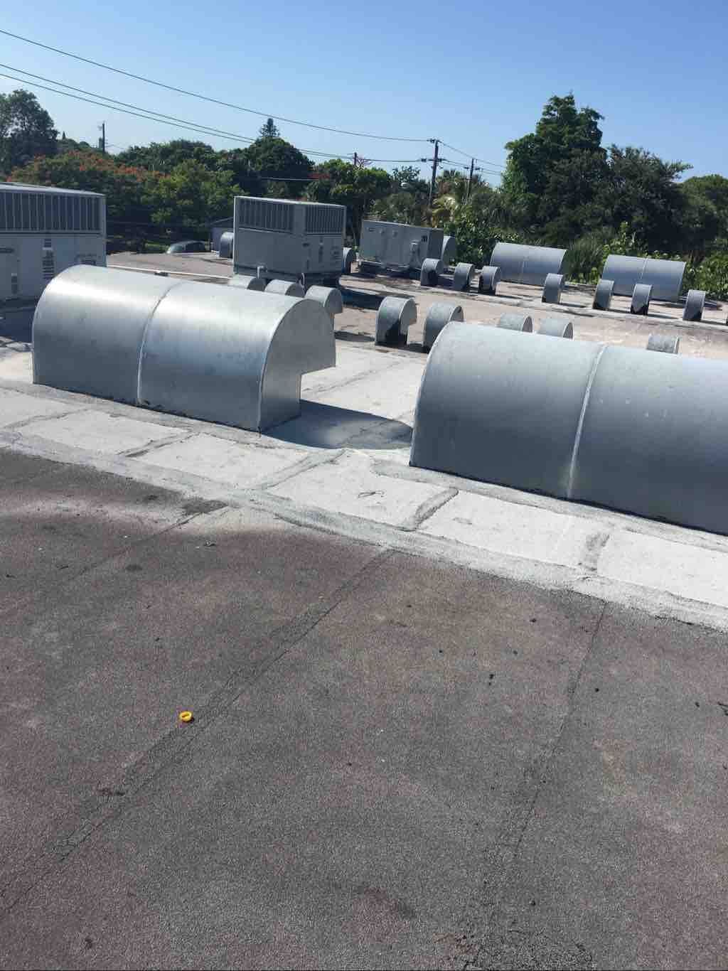 Rows of curved, metallic industrial ventilation hoods situated on a flat rooftop against a clear blue sky.