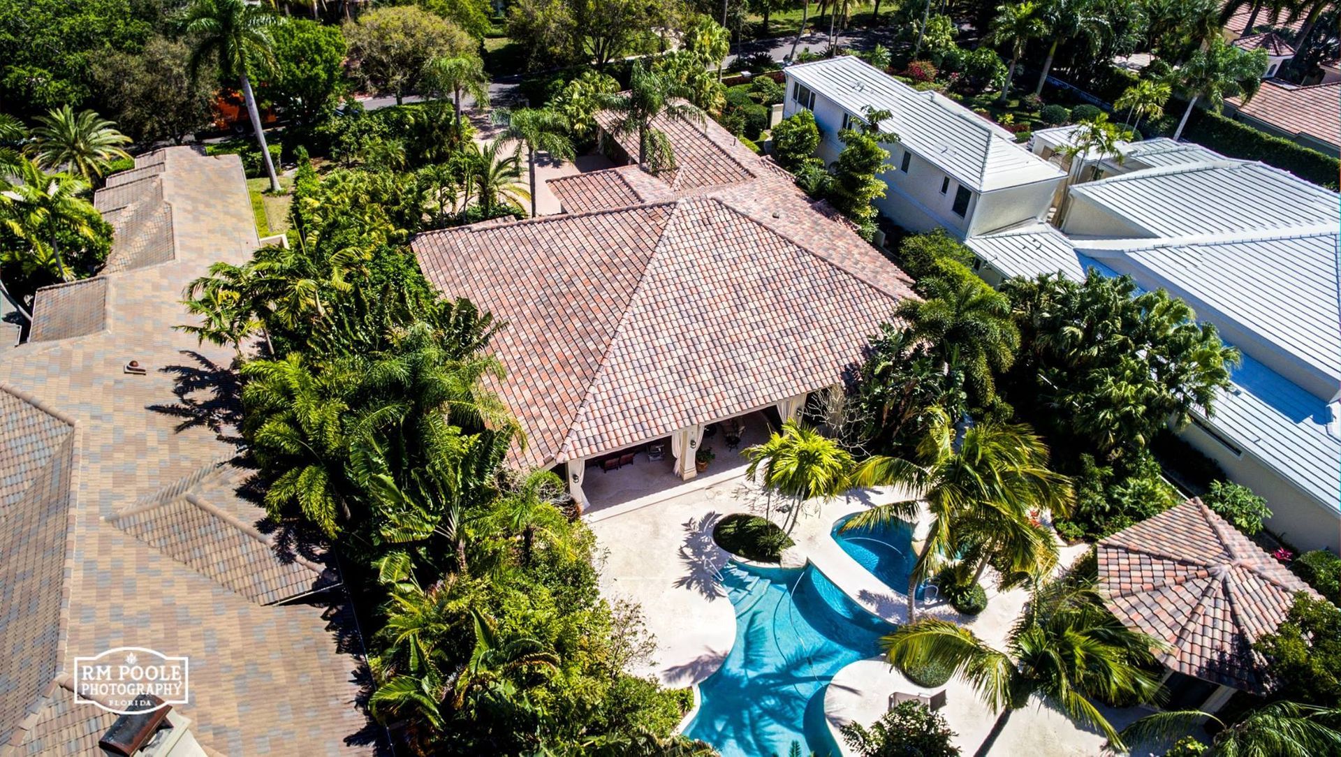 An aerial view of a luxury house with a tiled roof, surrounded by lush tropical greenery and a swimming pool.