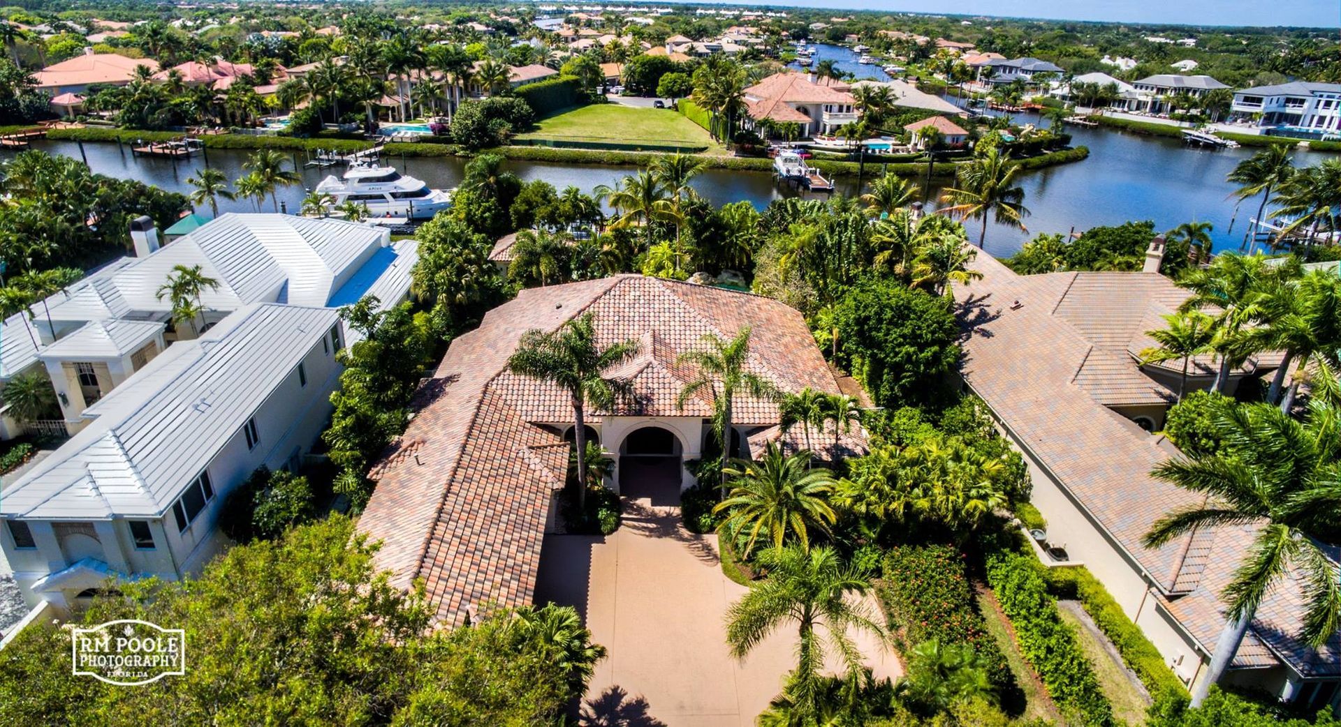 Aerial view of a coastal neighborhood with large houses, palm trees, and a canal with a moored boat.