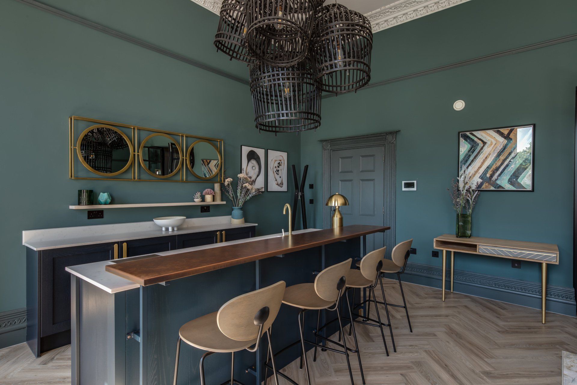 A kitchen with a long counter and stools and a chandelier hanging from the ceiling.
