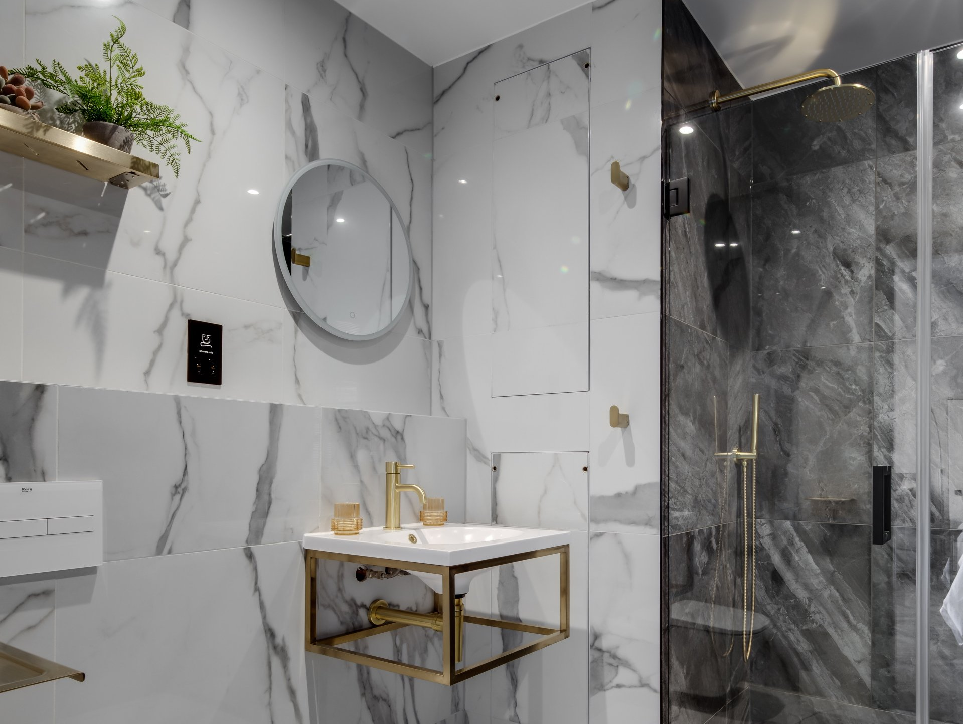 A bathroom with marble tiles , a sink , a mirror and a walk in shower.