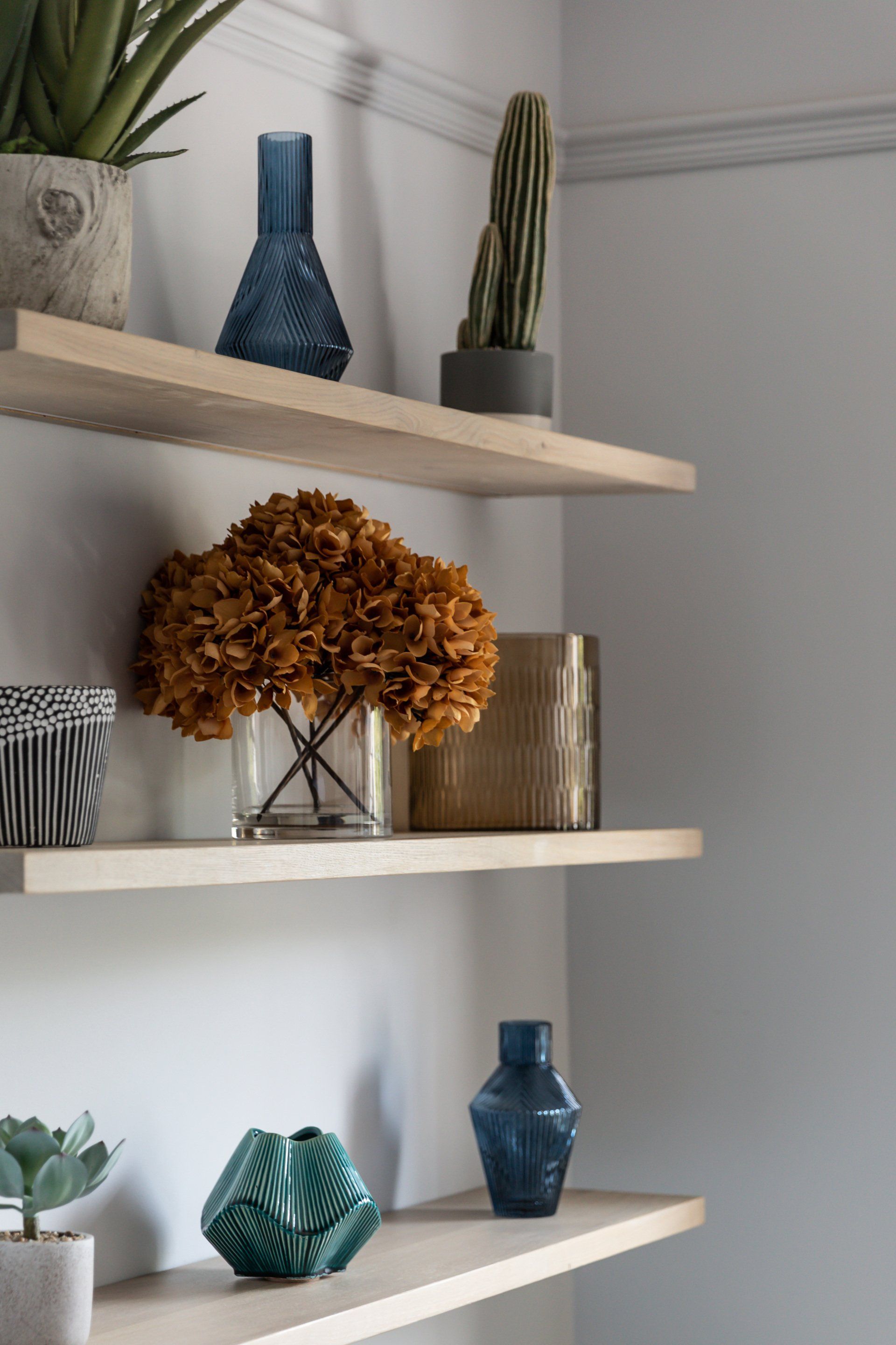A shelf filled with vases and plants on a wall.
