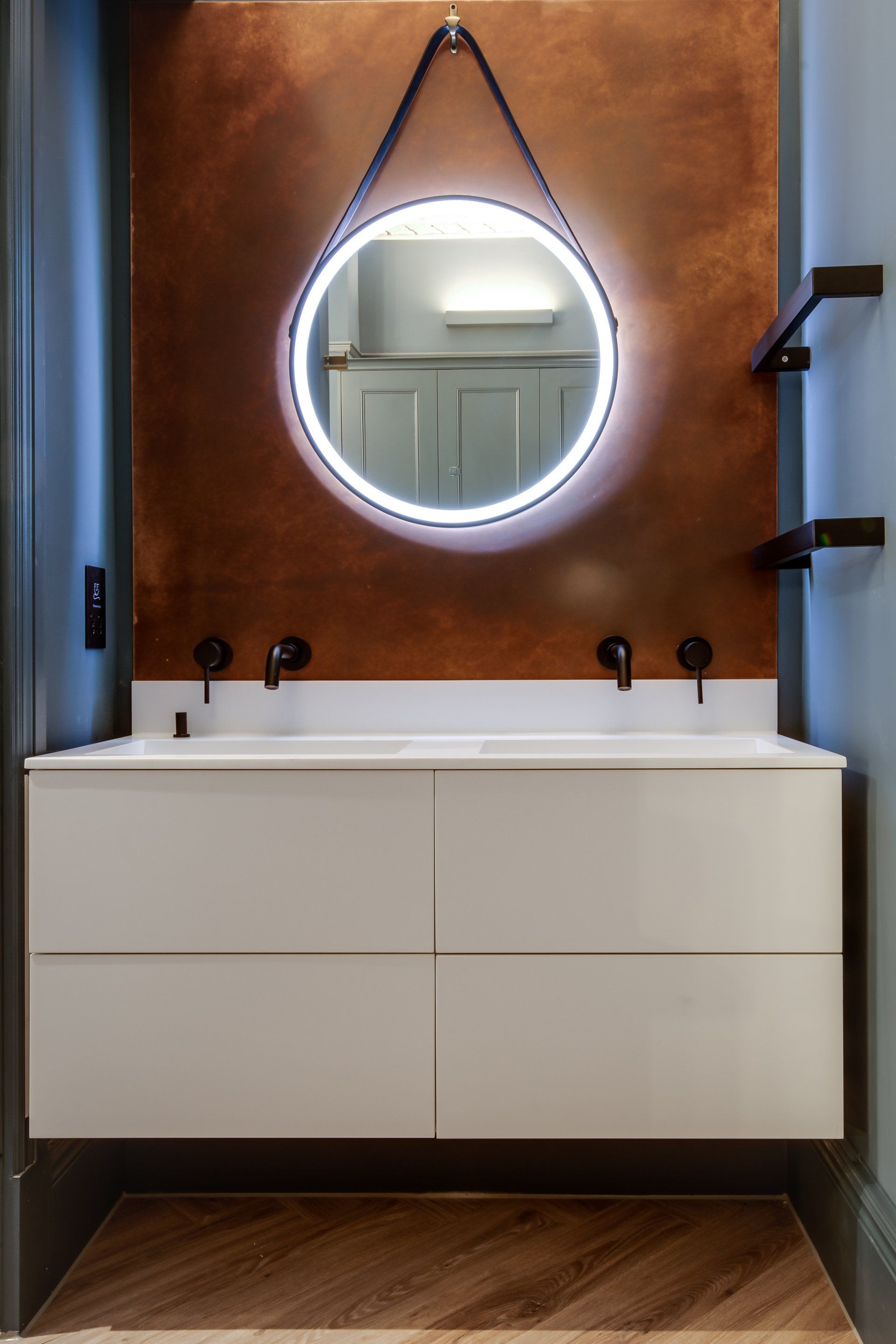 A bathroom with two sinks and a round mirror hanging from the wall.