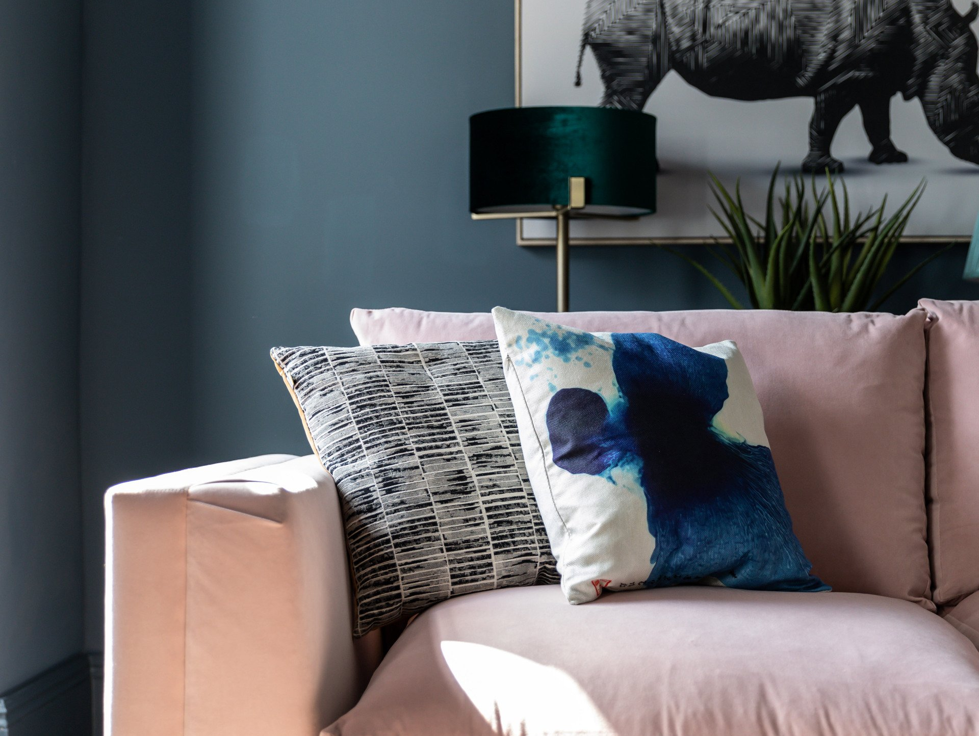 A pink couch with a picture of a rhino on the wall behind it