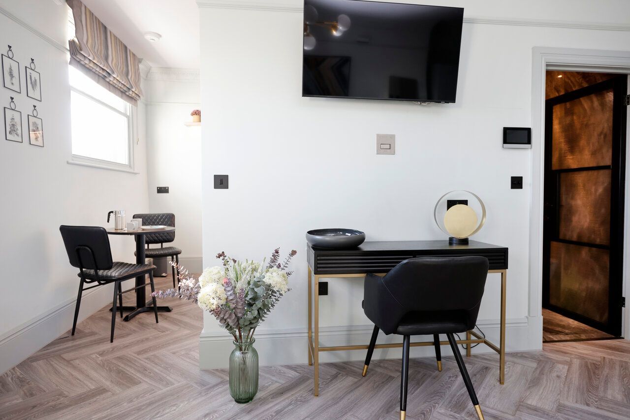 A living room with a desk , chair , television and a vase of flowers.