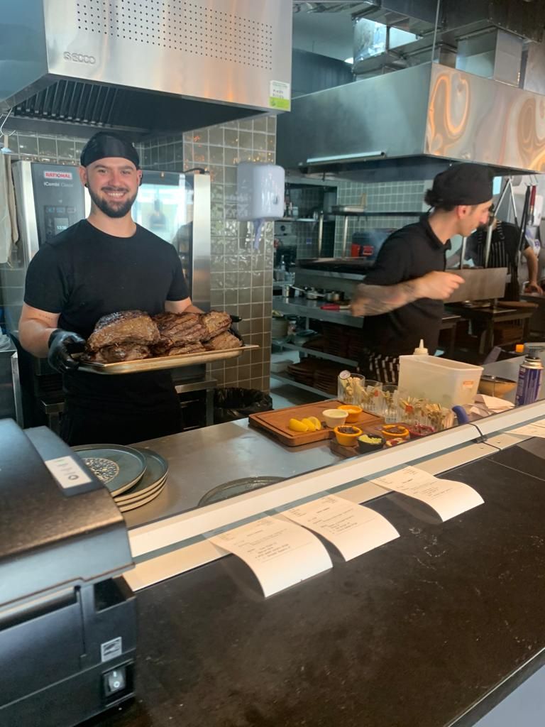 Two men are standing in a kitchen holding a tray of food.