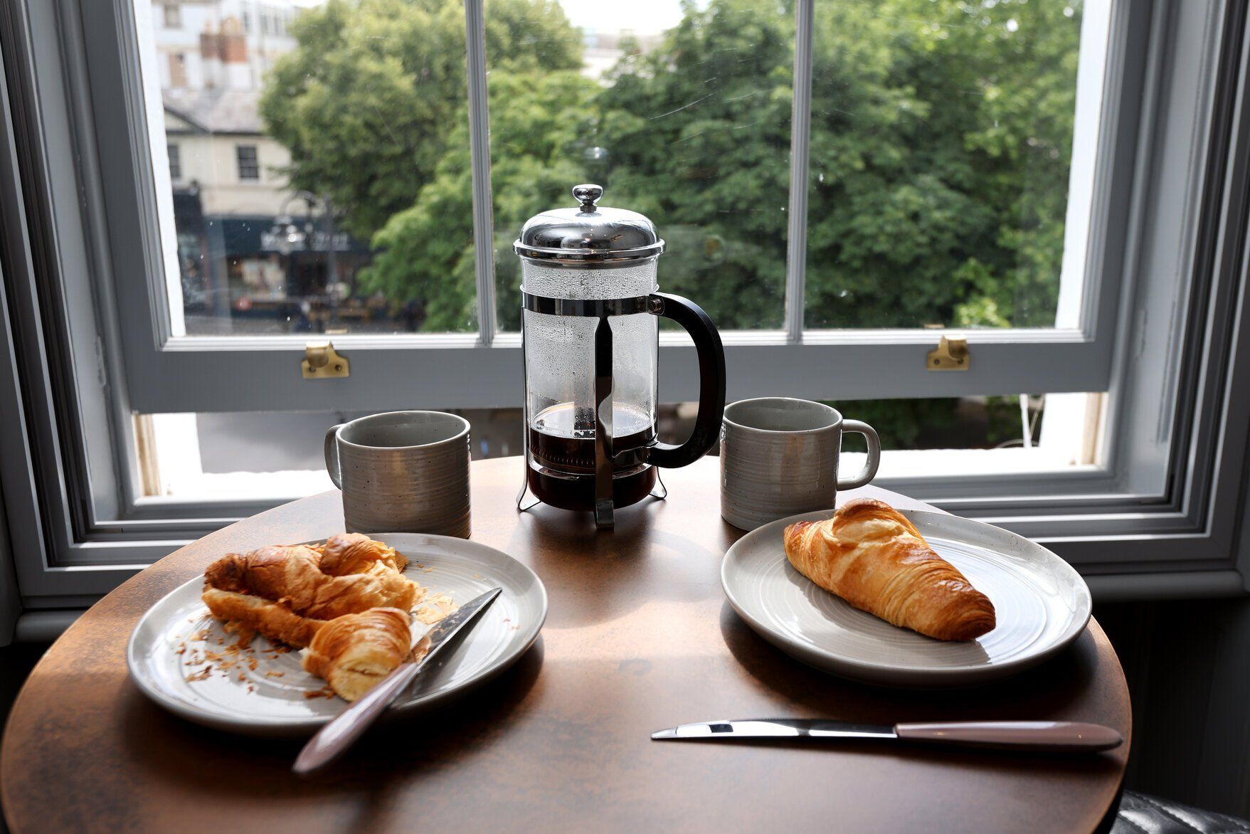 A table with two plates of food and a coffee pot in front of a window.