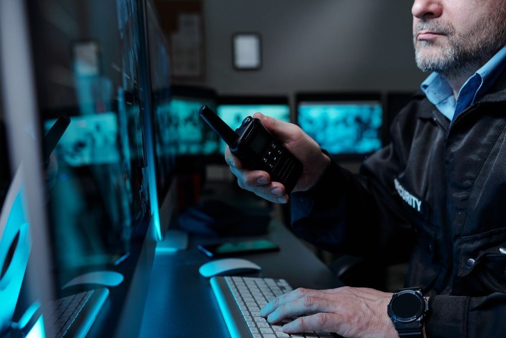 A man is sitting in front of a computer holding a walkie talkie.